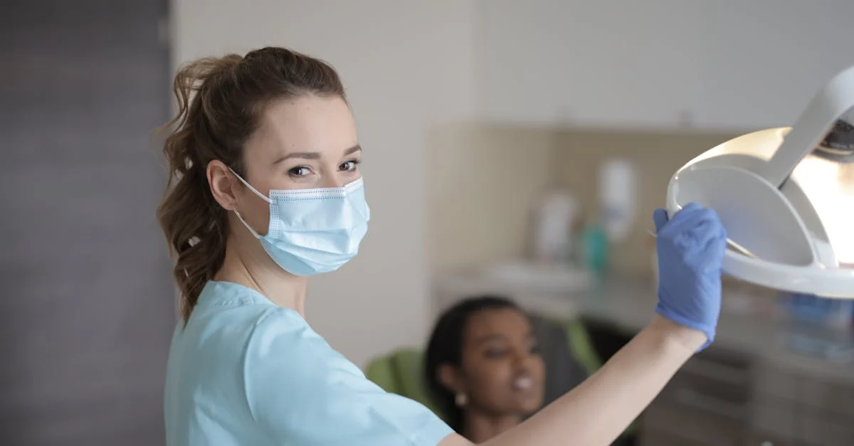 Female doctor wearing mask prepares lamp in clinic setting with patient.